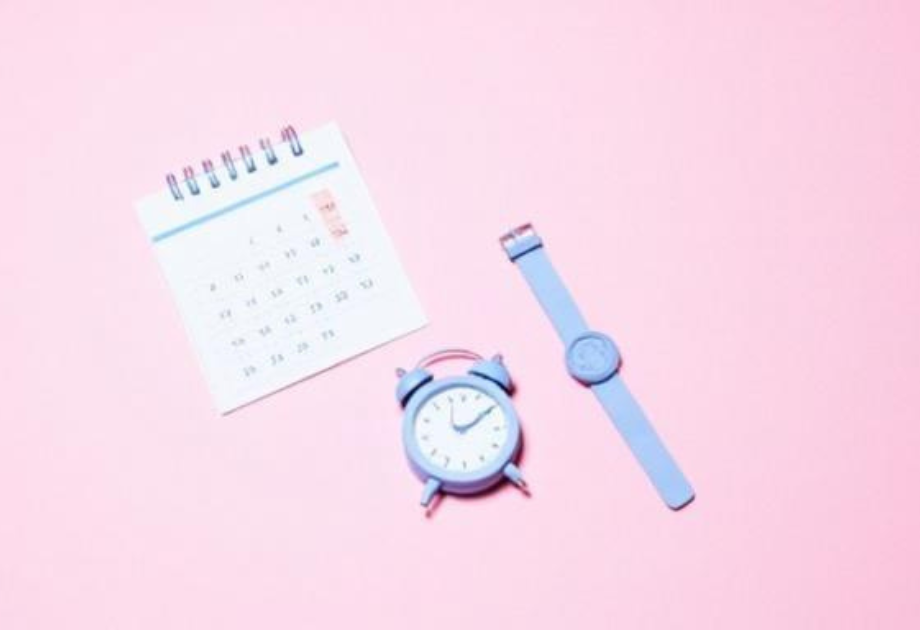 purple watch, purple alarm clock, and a paper calendar laid on a pink surface
