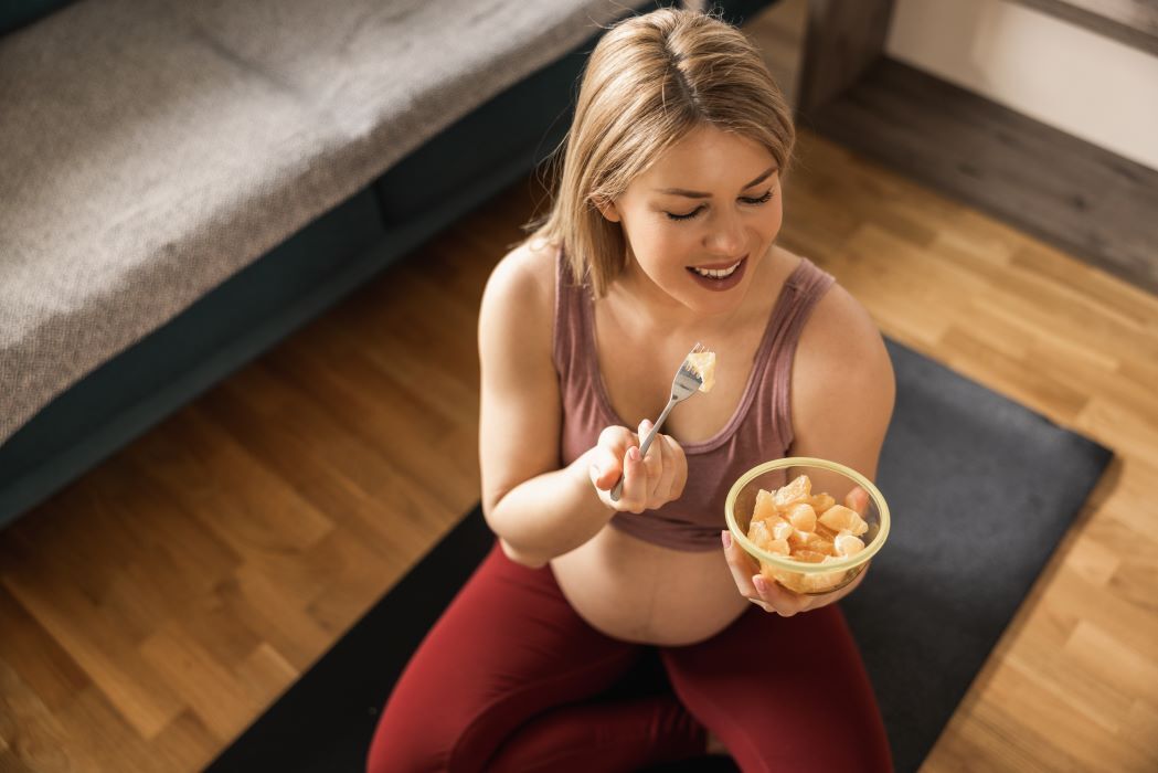 woman sitting on yoga mat, eating a bowl of fruit
