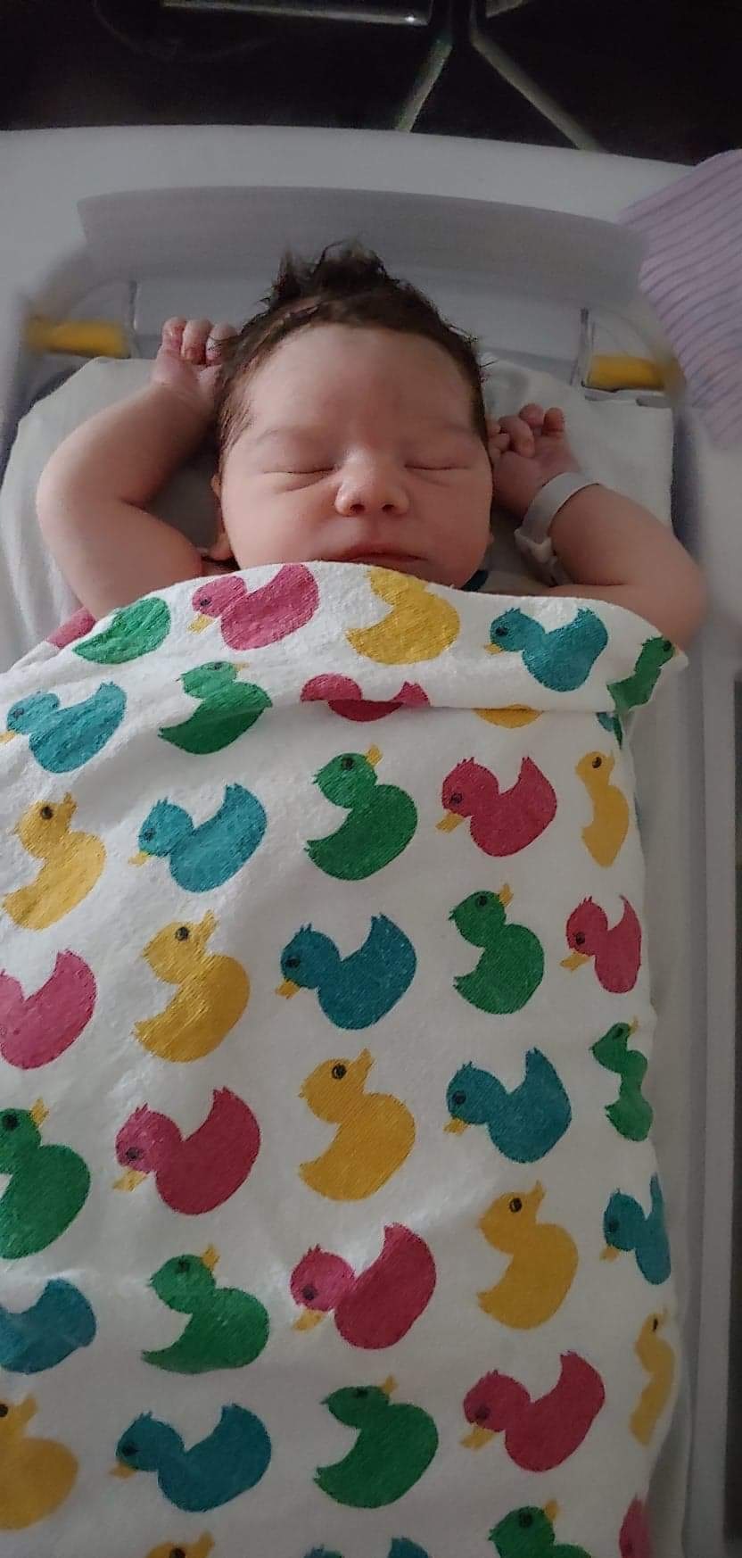 a baby laying in a bassinet with its arms up next to its head with a duck pattern blanket