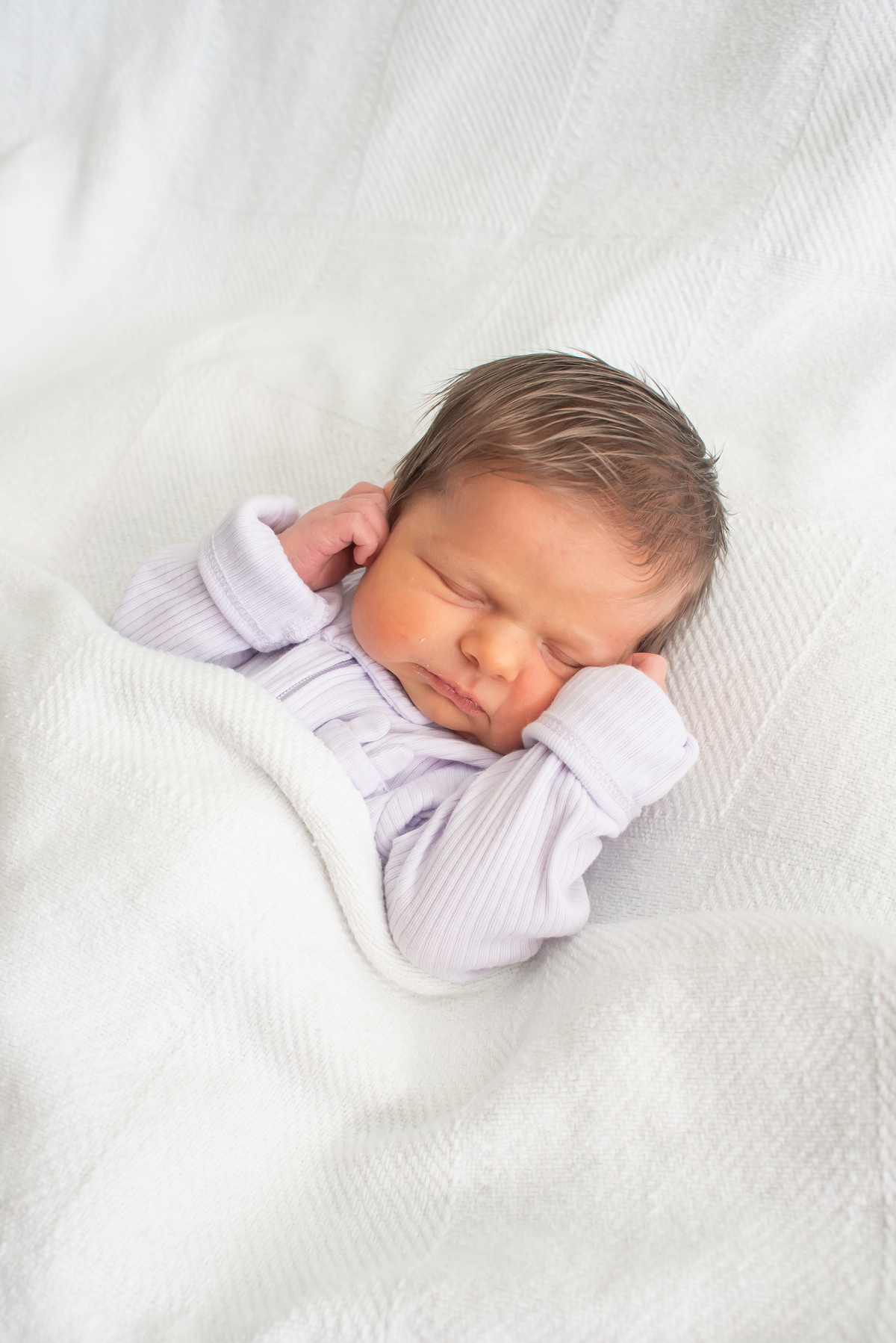 a baby sleeping on white blankets with its hands touching its face